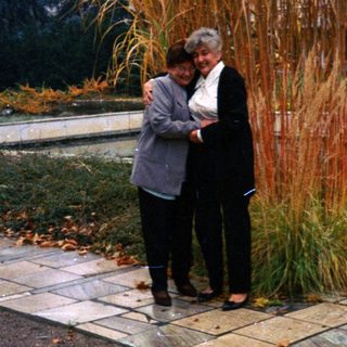 Two women stand near tall grass in a park.