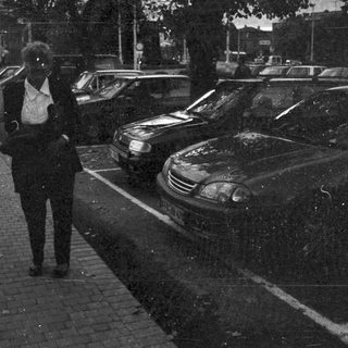 Person walking past parked cars on a dark street.