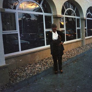 Man stands outside building with arched windows and landscaping.