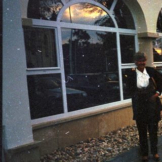 Man stands outside building with arched windows and landscaping.