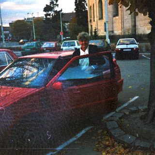 Parked cars line a street with a building in background.