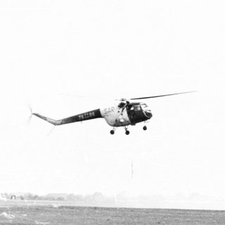 Helicopter hovers over a grassy field and runway.
