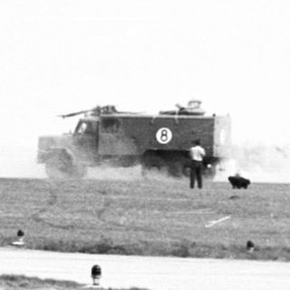 Helicopter hovers over a grassy field and runway.