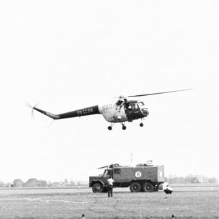 Helicopter hovers near a truck on a grassy field.
