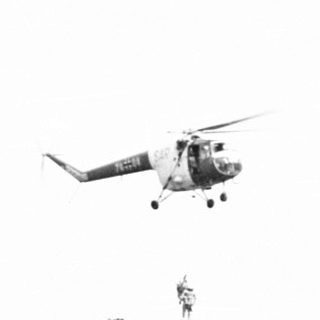 Helicopter landing near military vehicles and personnel.