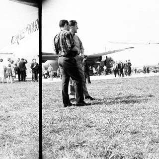 People observing an airplane on a grassy airfield.