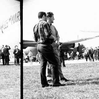 People observing an airplane on a grassy airfield.