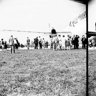 Group of people observing an airplane on a grassy field.