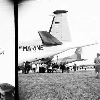 Crowd gathers near a Marine transport plane on grass.