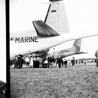 Crowd gathers near a Marine transport plane on grass.