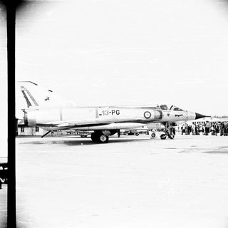 Fighter jet on runway with spectators gathered nearby.