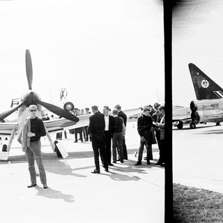 Group observes a propeller-driven aircraft on an airfield.