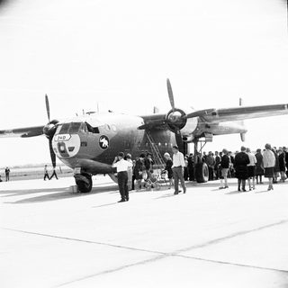 Military transport plane on tarmac with onlookers observing.