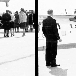 Military transport plane on tarmac with onlookers observing.