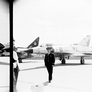 Pilot stands near a military aircraft on an airfield.