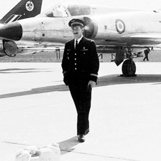 Pilot stands near a military aircraft on an airfield.