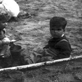 Three children play in a sandbox outdoors.
