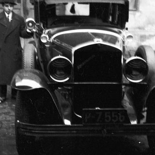 Vintage car with a driver, partially visible in black and white.