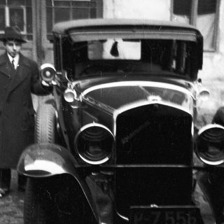 Vintage car with a driver, partially visible in black and white.