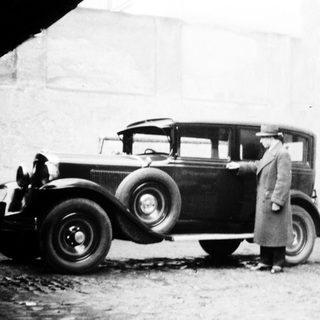Man stands next to a vintage car near a building.