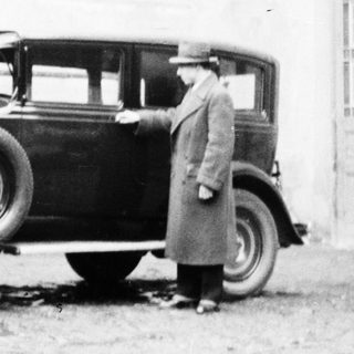 Man stands next to a vintage car near a building.