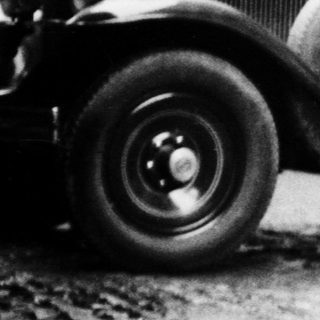 Man stands next to a vintage car near a building.