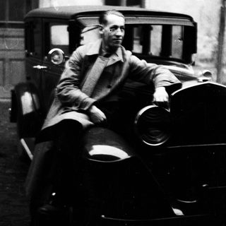 Man seated on vintage car, leaning against it.