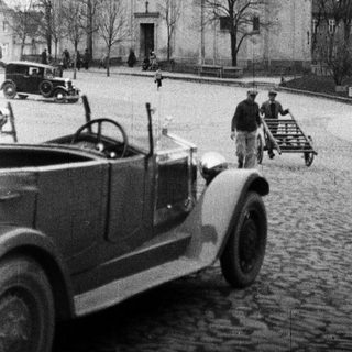 Vintage car near a church and people in a square.