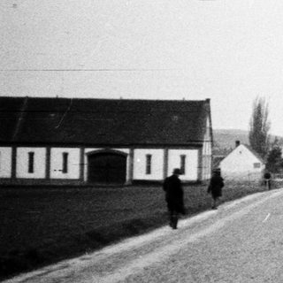 Road leads toward village with people and distant hill.