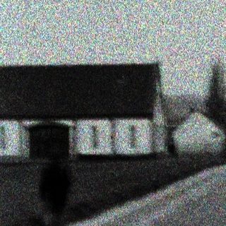 Monochrome image depicting a road, buildings, and utility poles.