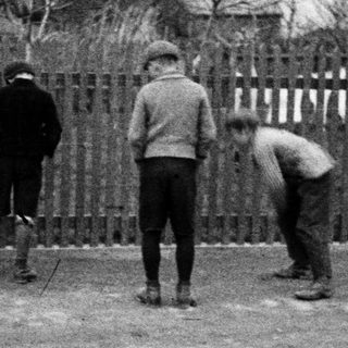 Three boys stand behind a wooden fence in a yard.
