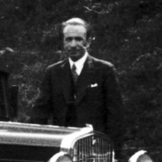 Man stands next to a vintage car on a road.