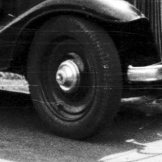 Man stands next to a vintage car on a road.