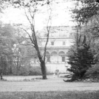 A stately mansion viewed through trees in a park.