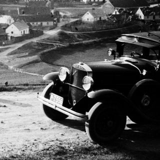 Vintage car overlooks a village in a rural landscape.
