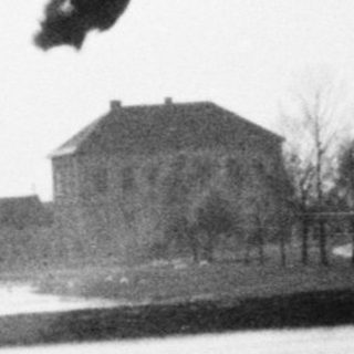 Black and white image of a lake with buildings across.