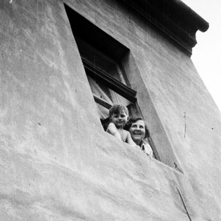 Children peering from a window in a textured wall.