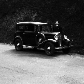 Vintage car and man standing beside it on a road.
