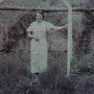 Here's a brief summary of the image: Person stands near a weathered structure in a grassy area.