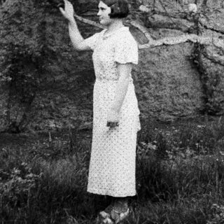 Woman in dress stands near a tree in a field.