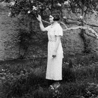 Woman in dress stands near a tree in a field.