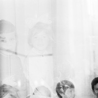 Here's a brief summary of the image: Children peering through a window, appearing ghostly and blurred.