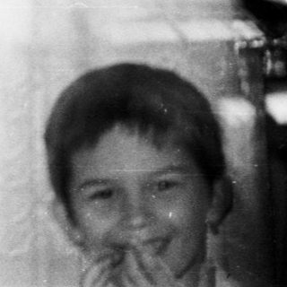 Here's a brief summary of the image: Children peering through a window, appearing ghostly and blurred.