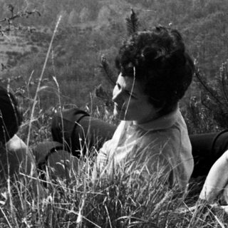 Three women seated in tall grass with a hilly landscape.
