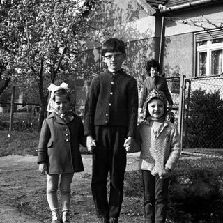 Three children standing outside a house in a black and white photo.