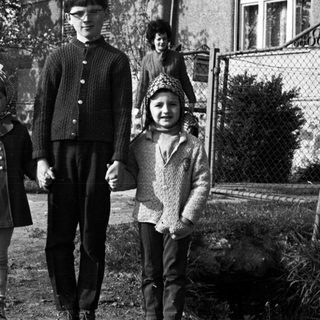 Three children standing outside a house in a black and white photo.
