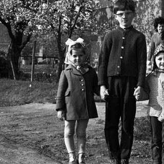 Three children standing outside a house in a black and white photo.