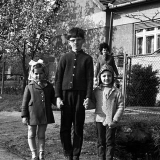Three children standing outside a house in a black and white photo.
