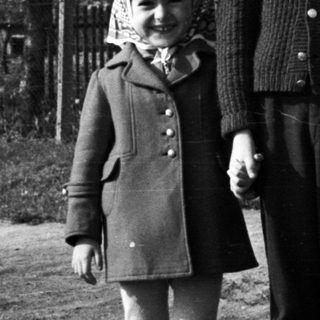Three children stand together outside a house in black and white.