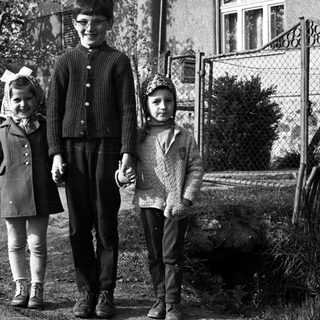 Three children stand together outside a house in black and white.